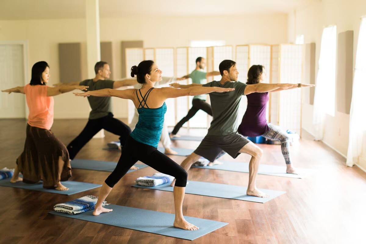 Guests holding a warrior pose in a sunlit yoga class